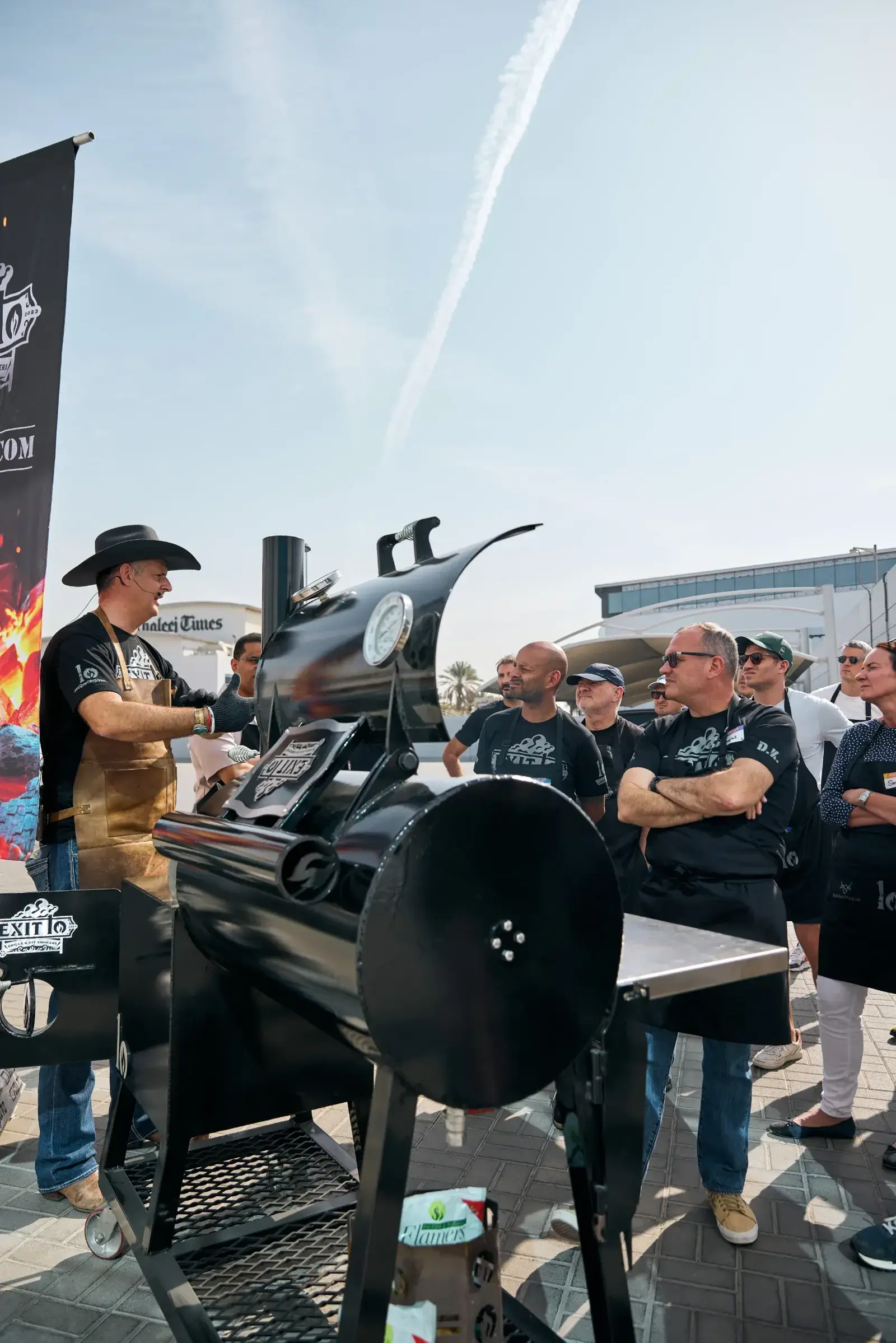 Pitmaster Dave spraying a brisket on the smoker while Pitmaster Hunter points out the bark to students at the Exit 10 masterclass